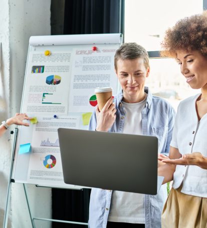 Diverse group of hard-working businesswomen standing around a laptop in a coworking space.