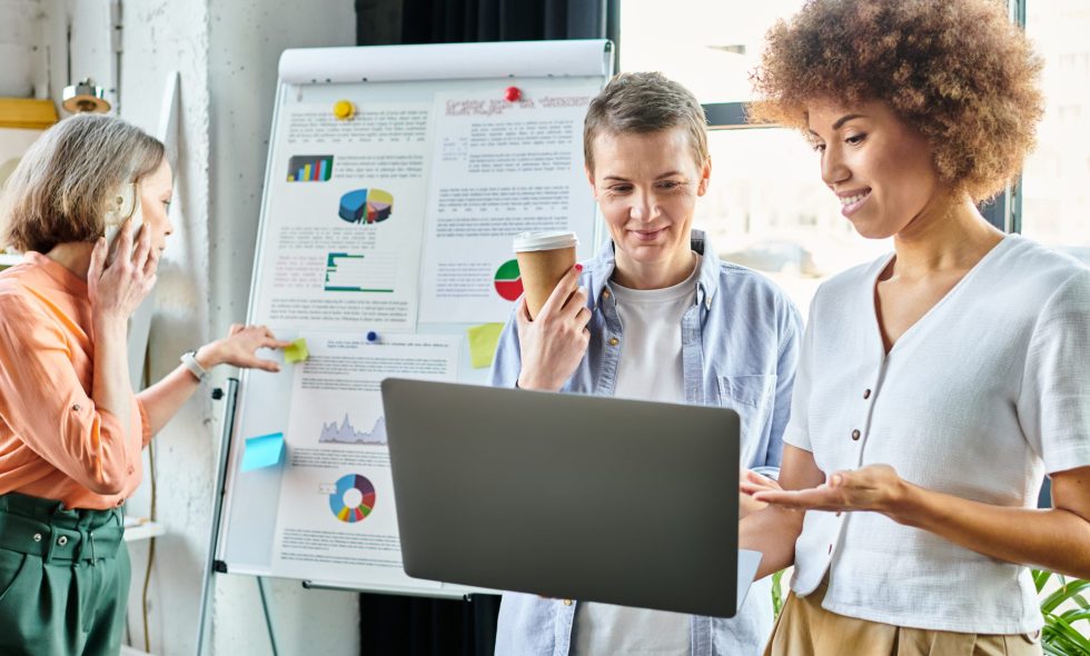 Diverse group of hard-working businesswomen standing around a laptop in a coworking space.