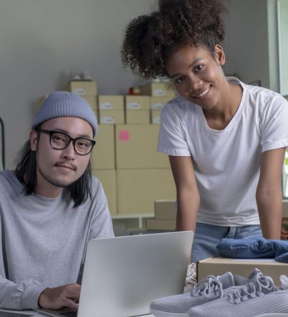 Two small business owners buy a domain name on laptop while working on product.
