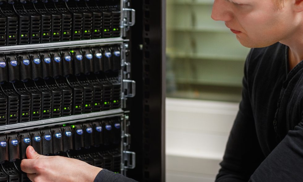Cloud server manager employee works on datacenter storage device, performing maintenance.